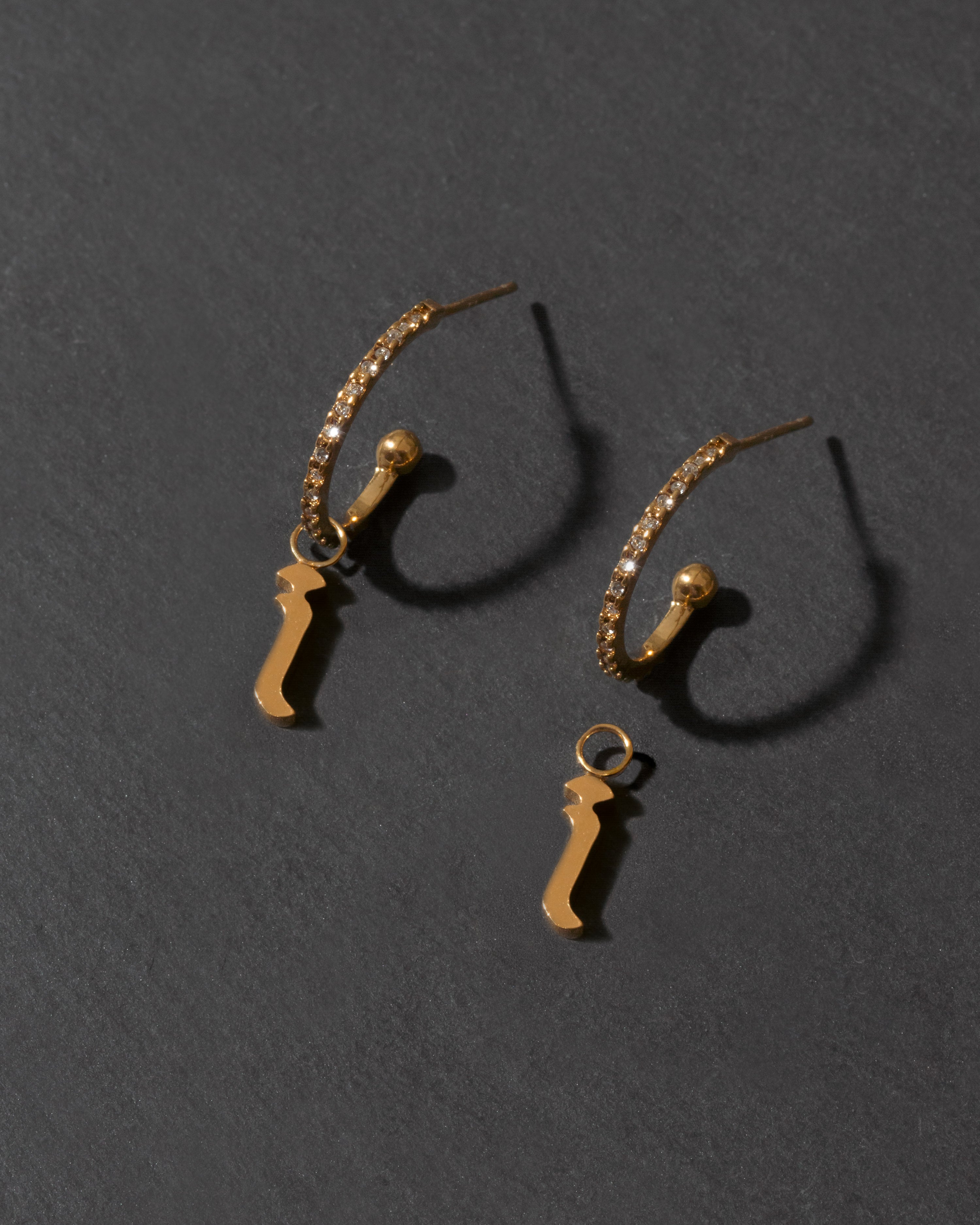 Pair of gold letter "i" earrings on a dark gray background