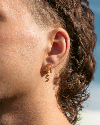 Close-up of an ear with gold earrings against a blurred natural background