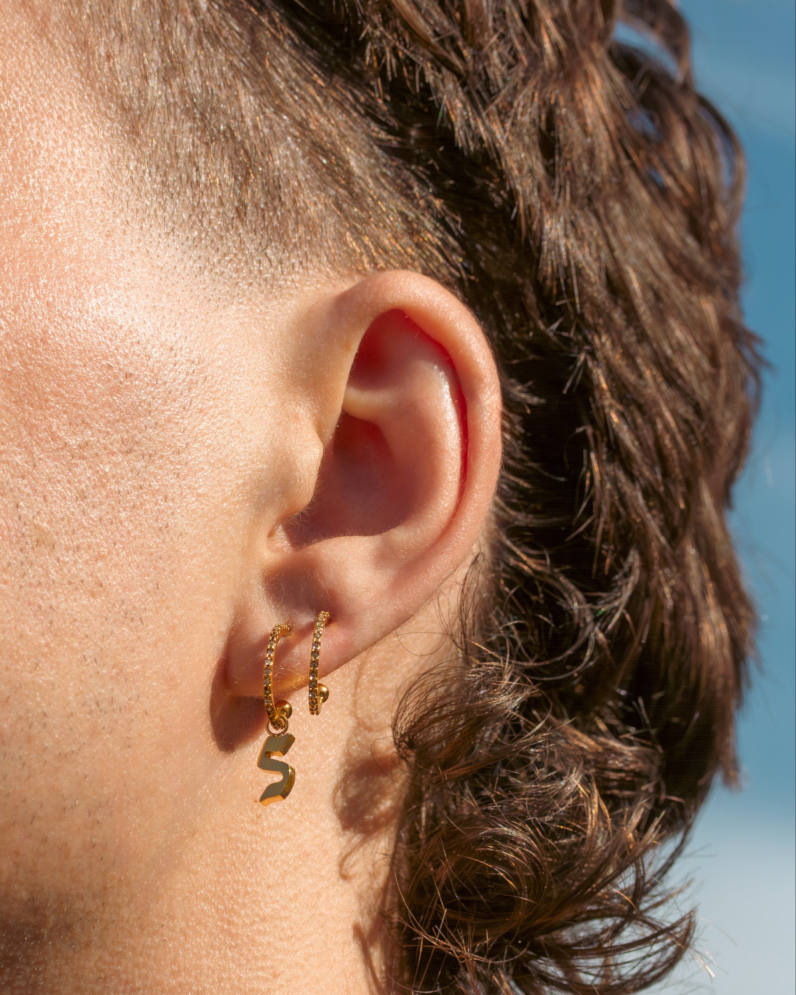 Close-up of an ear with gold earrings against a blurred natural background