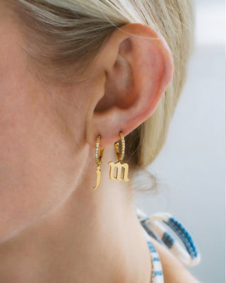 Person wearing gold initial hoop charms earrings with coordinating CZ post hoops with letter 'J' and 'M' charms.