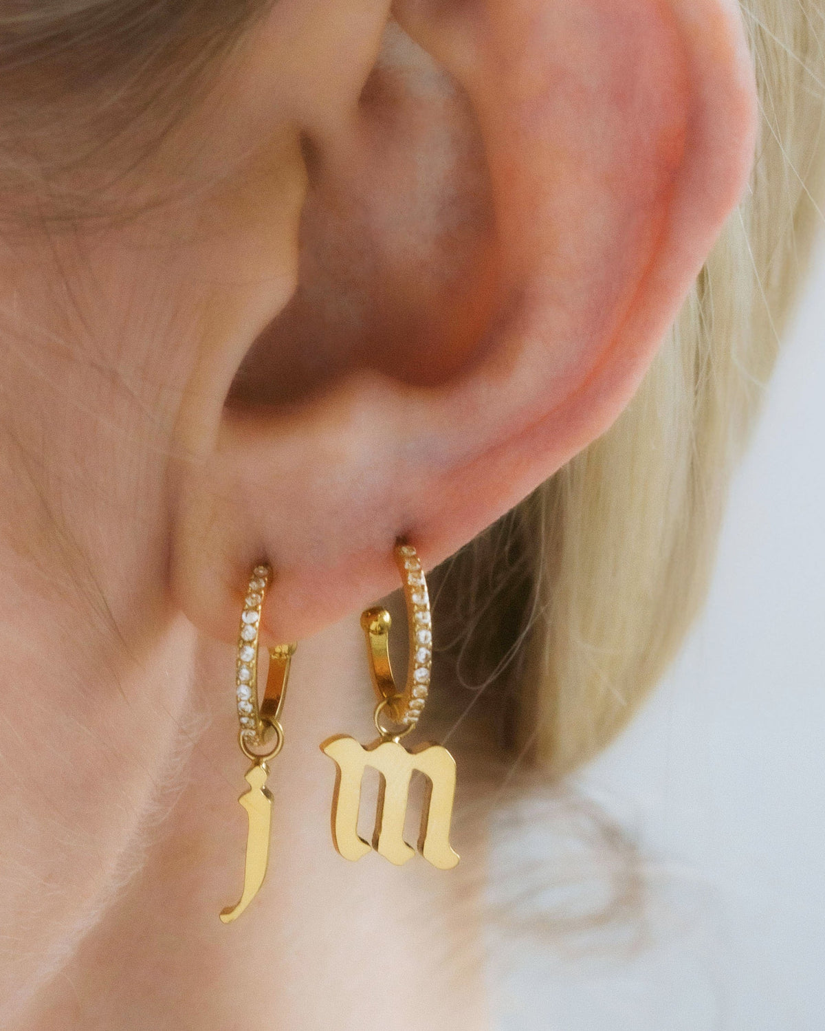 Person wearing gold initial hoop charms earrings and CZ post hoops with letter 'J' and 'M' charms.
