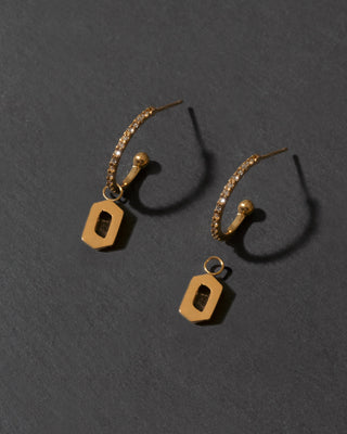 Pair of gold earrings with letter 'o'  on a dark gray background