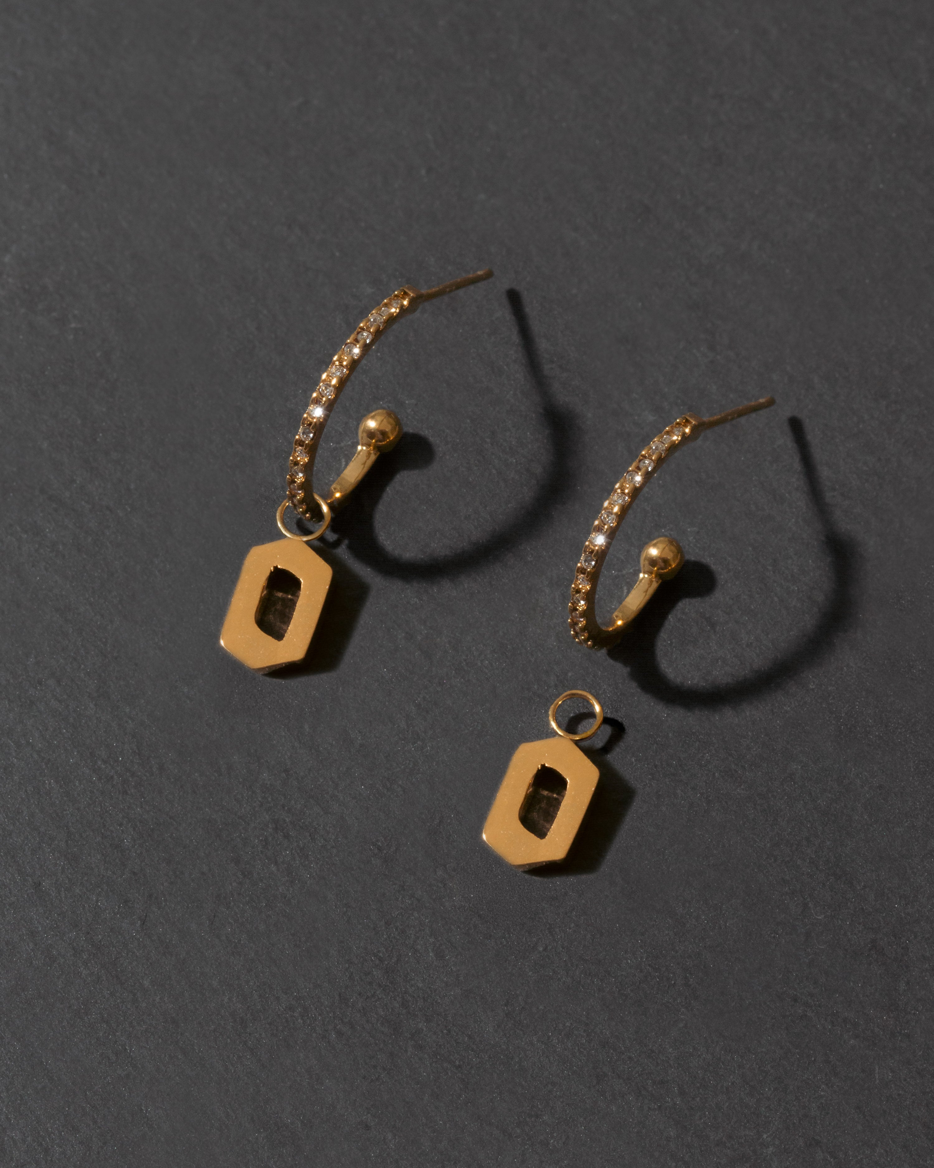 Pair of gold earrings with letter 'o'  on a dark gray background
