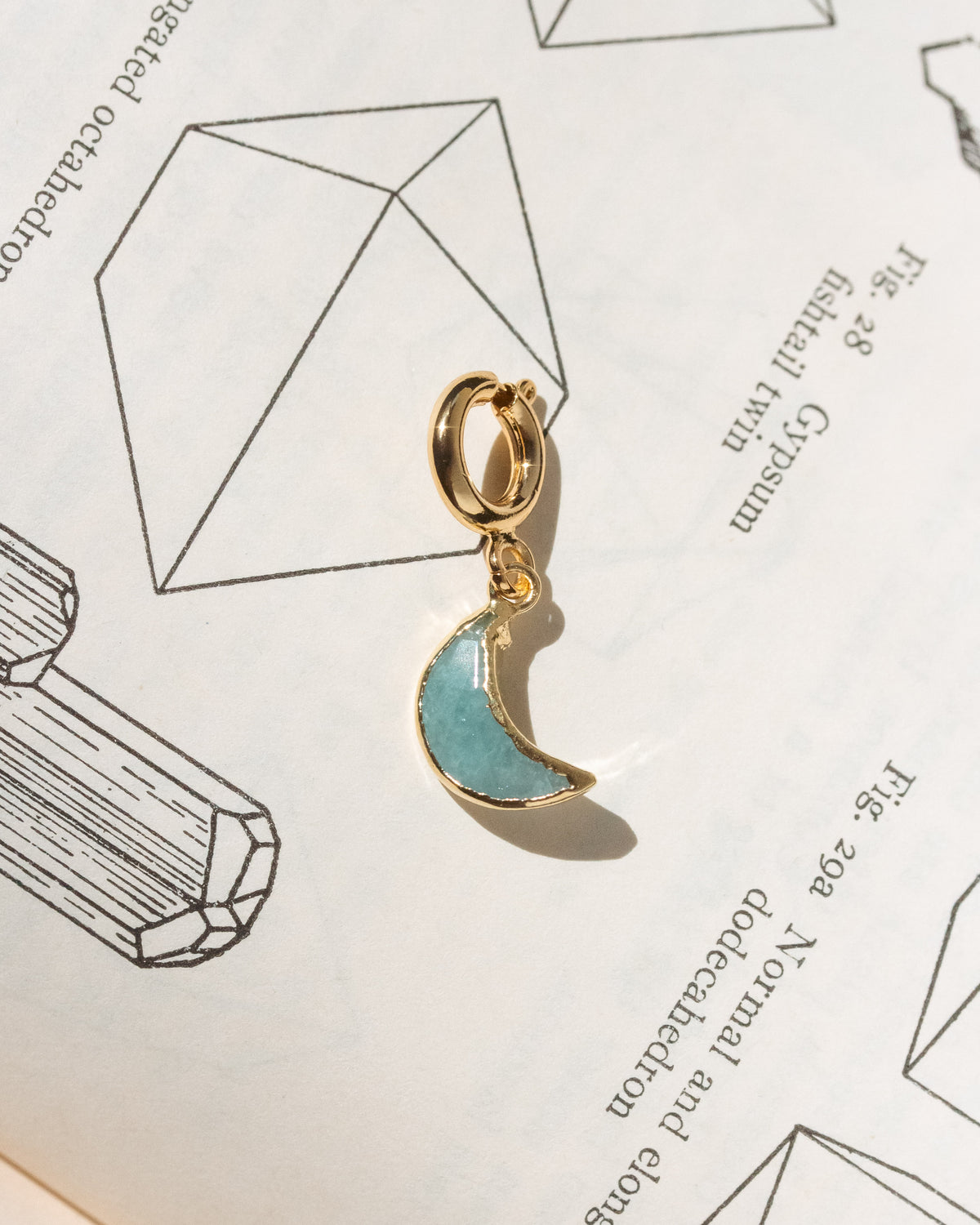 Gold and blue crescent moon charm on a white background with geometric designs.