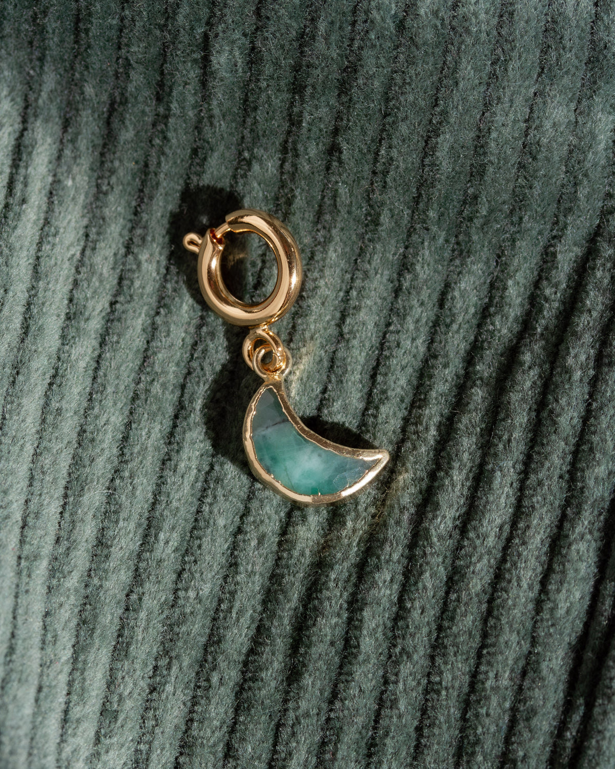 Gold and green moon charm on a textured green background