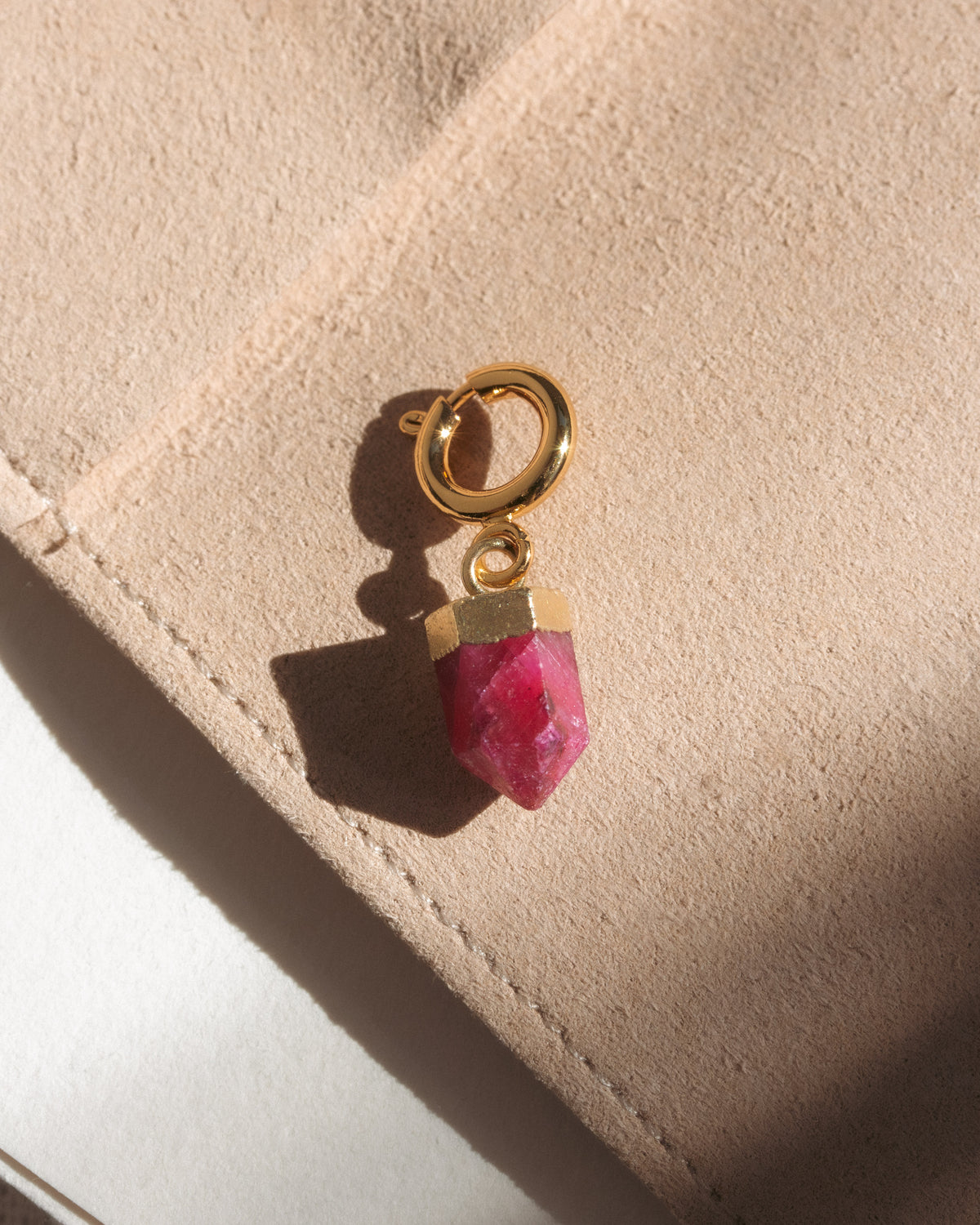 Gold charm with a pink gemstone on a beige surface