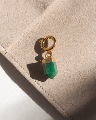 Gold earring with a green gemstone on a beige surface