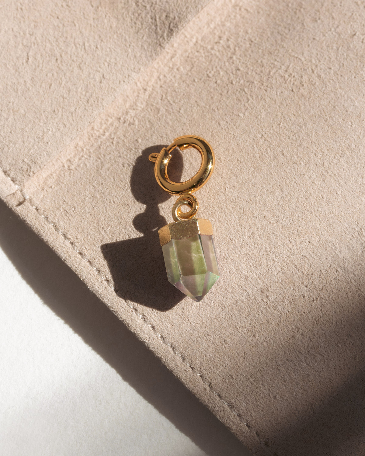 Gold c-clasp charm with a multicolor crystal on a beige surface