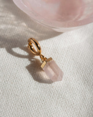 Gold charm with a pink crystal on a light fabric background