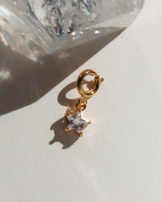 Gold charm with a star-shaped clear cz stone on a light background