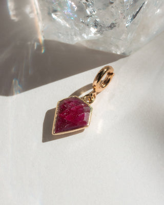 Gold pendant with a red gemstone on a white surface