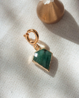 Gold charm with a green stone on a white fabric background