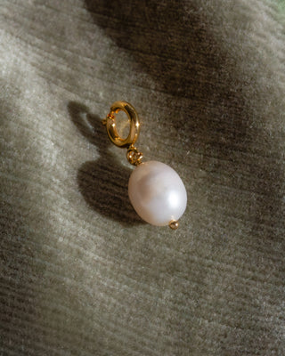 Pearl charm on a gold clip against a textured gray background