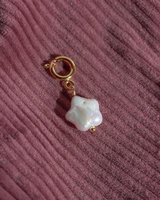 Pearl charm with gold clasp on a textured pink surface