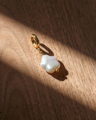 Pearl charm on a gold clasp against a wooden background