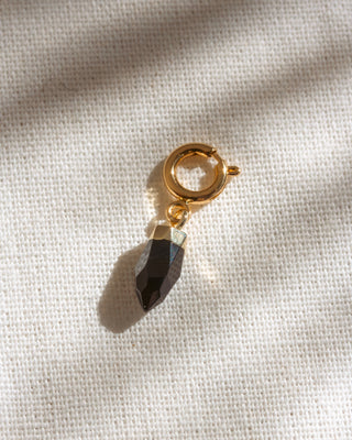 Gold charm with a black stone on a beige fabric background