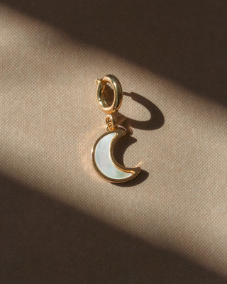 Gold charm with a moon-shaped pendant on a beige fabric background