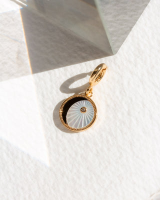 Gold and black circular moon pendant on a white textured surface