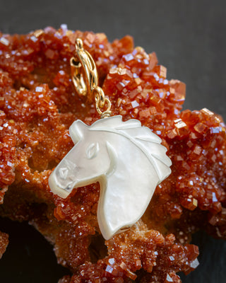 White mother-of-pearl horse head charm on gold c-clasp against a red crystal background