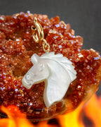 White mother-of-pearl horse head charm on gold c-clasp against a fiery red crystal background
