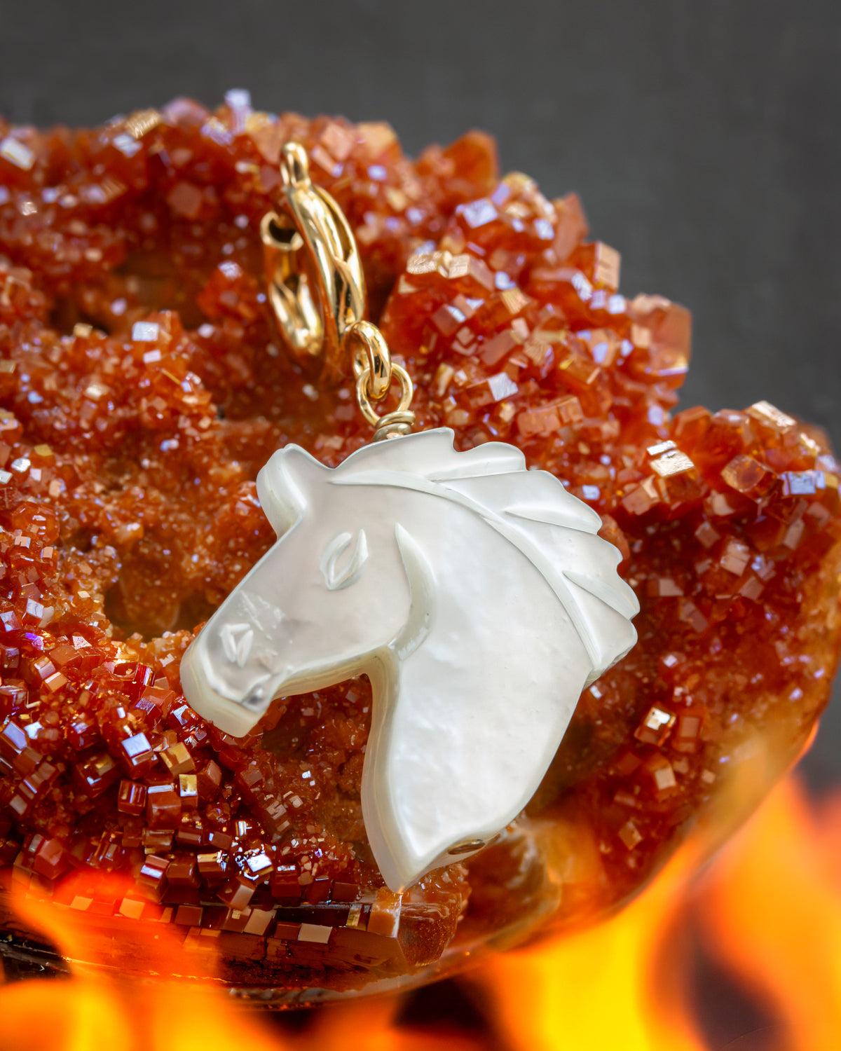 White mother-of-pearl horse head charm on gold c-clasp against a fiery red crystal background
