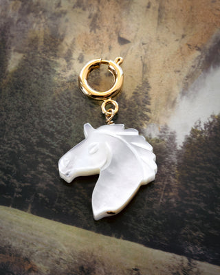 White mother-of-pearl horse head charm on gold c-clasp against a textured brown background
