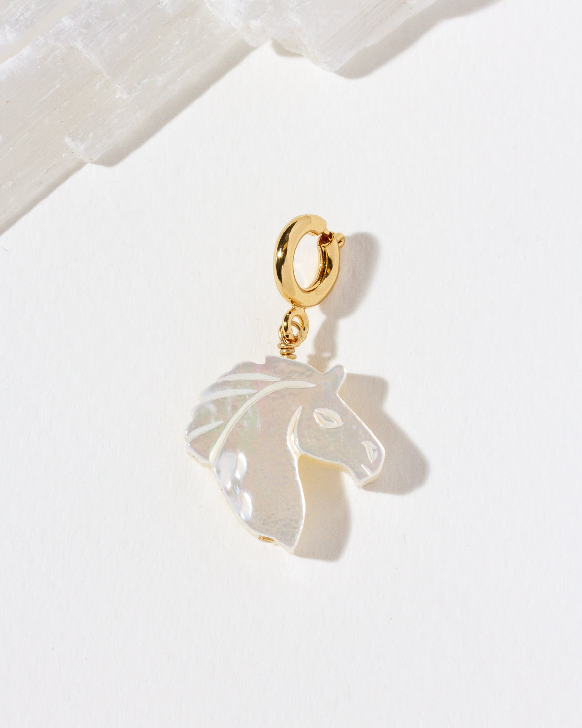 Mother-of-pearl horse head charm on gold c-clasp against a red white background