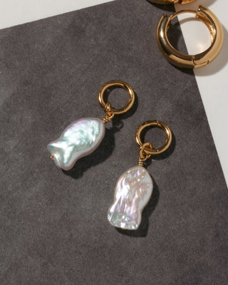Cultured freshwater pearl fish earring charms with gold loops on a dark surface