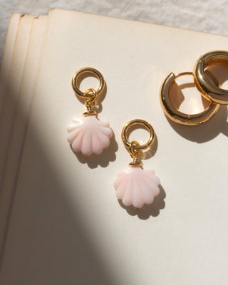 Pair of gold hoop earring charms with pink shells on a textured surface