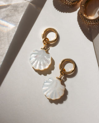 Gold earrings with shell-shaped charms on a light surface