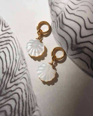 Shell-shaped earrings with gold charm rings on a textured surface