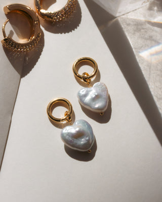 Gold hoop earrings with heart-shaped pearls on a light surface