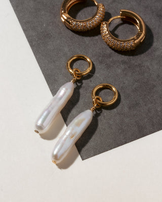 Gold hoop earrings with clear CZ stones and gold drop charm earrings with pearls on a gray and white background.