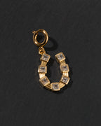 Gold c-clasp horseshoe charm with clear CZ embedded stones on a dark background