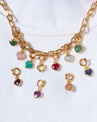 Gold chain necklace with multiple dangling heart charms in various colored stones, displayed on a white ribbed knit top.