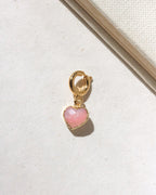 Gold charm with a pink heart-shaped stone on a light background