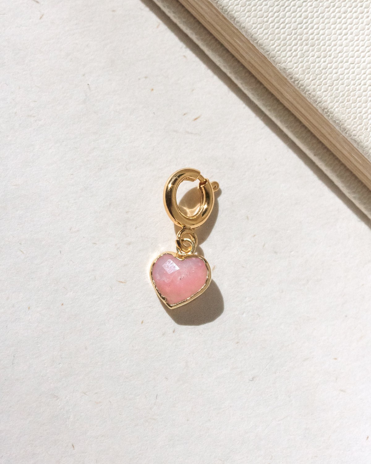 Gold charm with a pink heart-shaped stone on a light background