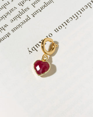 A small gold heart-shaped charm with a faceted red ruby gemstone.