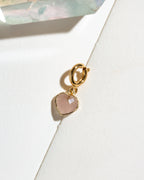 A gold heart-shaped charm with a faceted pale pink rose quartz stone.