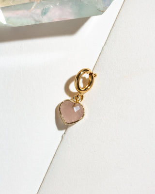A gold heart-shaped charm with a faceted pale pink rose quartz stone.