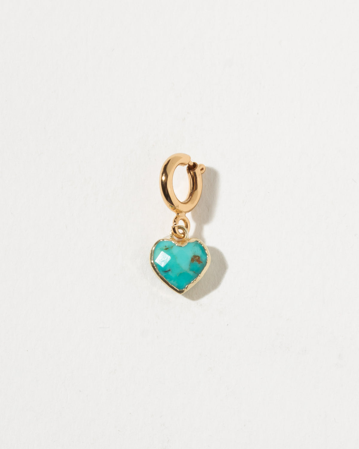 Gold heart-shaped pendant with turquoise stone on a light gray background