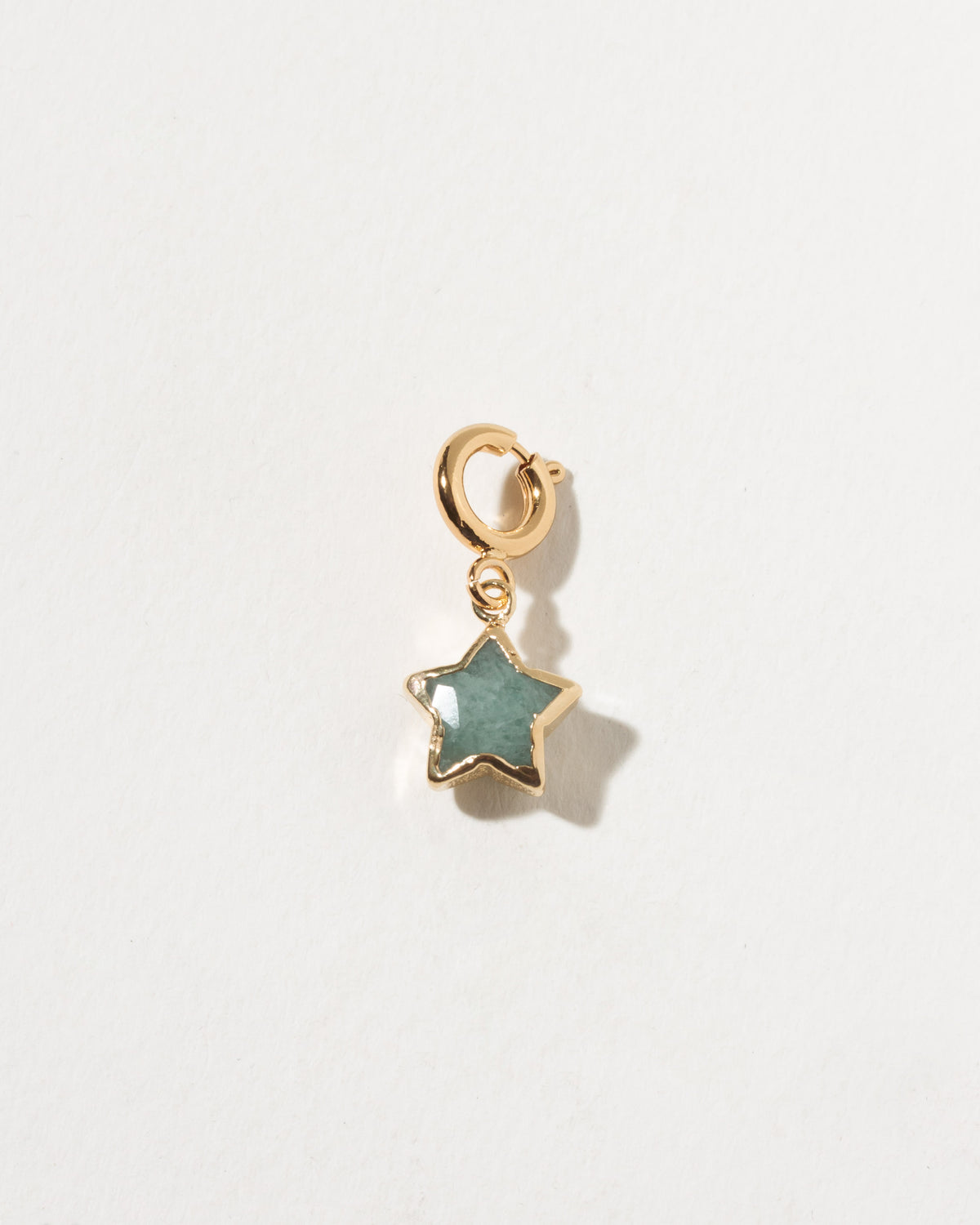 Gold star-shaped pendant with a green stone on a light gray background