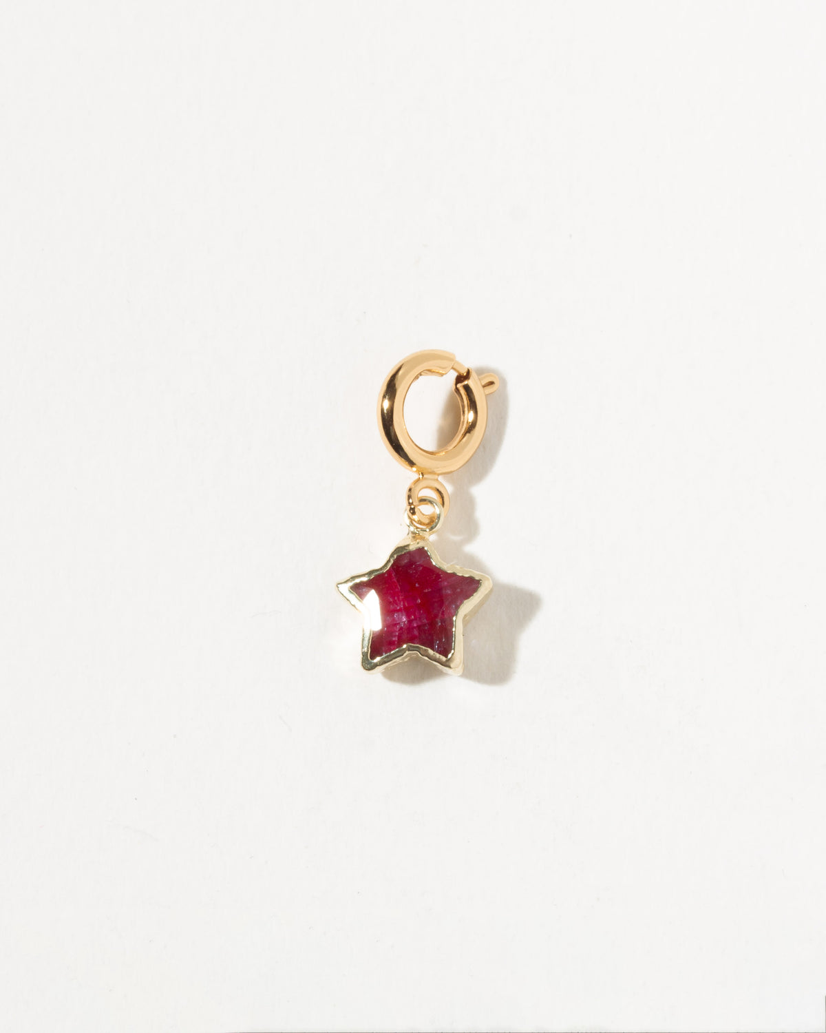 Gold charm with a ruby gemstone on a white background
