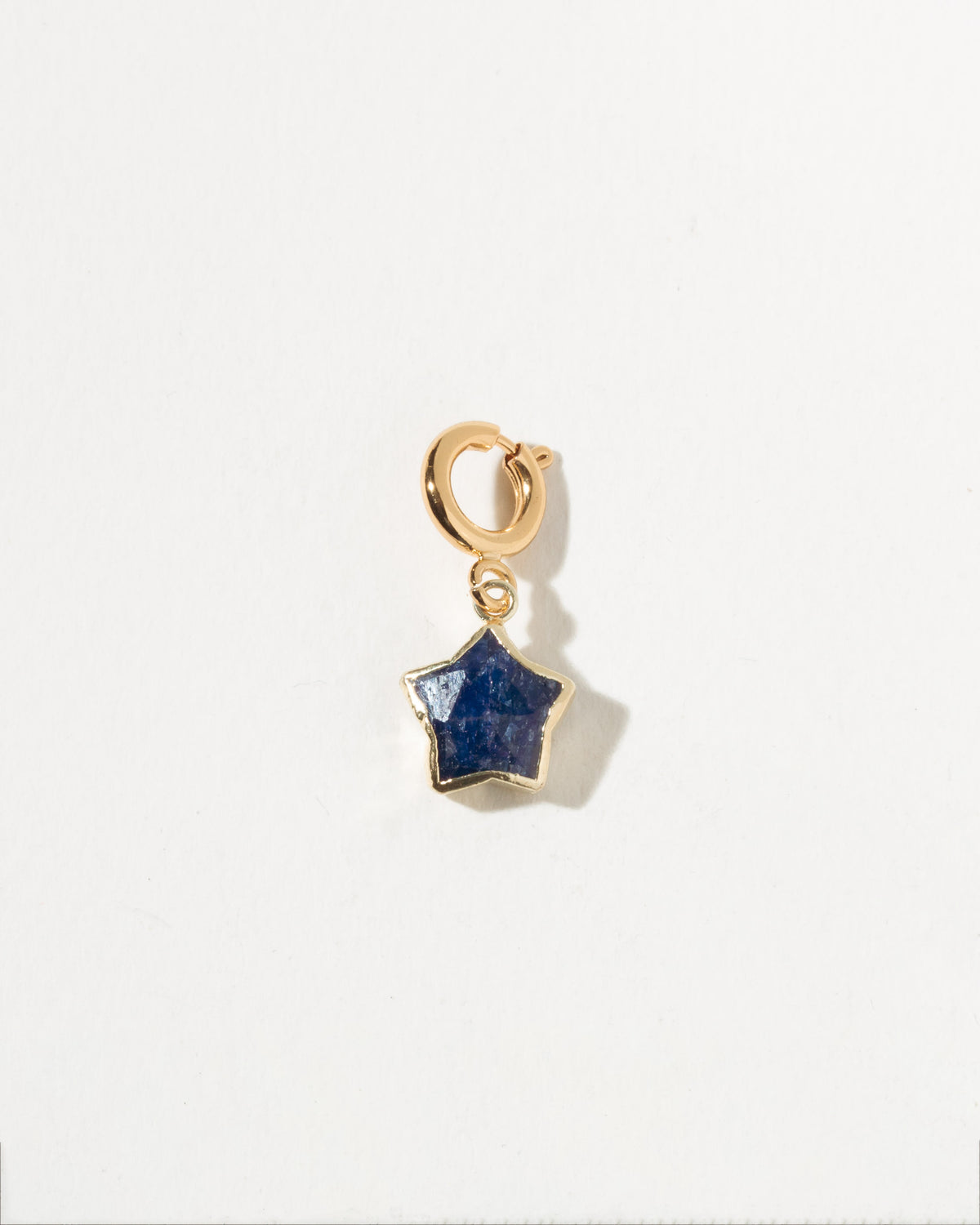 Gold charm with a blue star-shaped stone on a white background