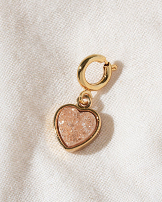 A gold heart-shaped peach druzy charm with a gold clasp.