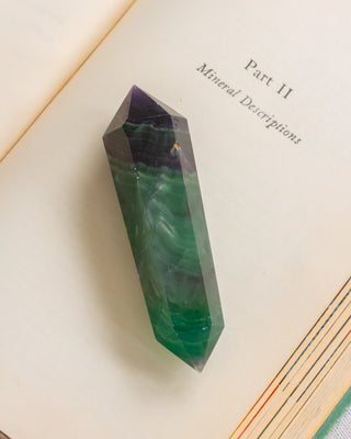 Green crystal on an open book with 'Part II Mineral Descriptions' text.