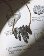 Rainy Day Necklace with black stones and a gold chain laying on a page with mineral illustrations.