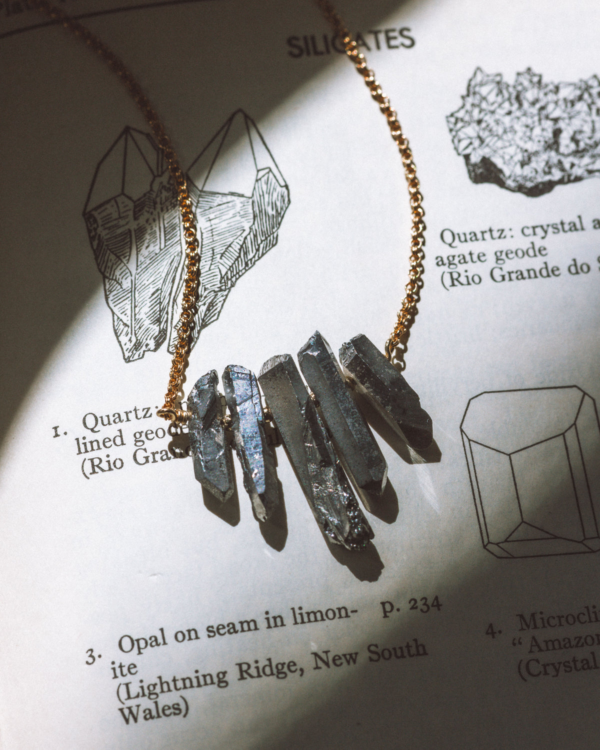 Rainy Day Necklace with black stones and a gold chain laying on a page with mineral illustrations.