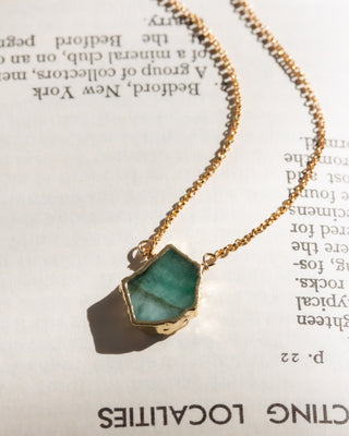 Gold chain necklace with a green emerald pendant on a book page