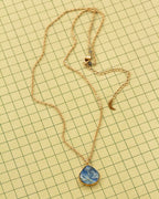 A gold chain necklace with a blue and white marbled kyanite teardrop shaped pendant, laid flat on a yellow grid background.